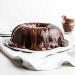 A chocolate frosting covered Chocolate Buttermilk Bundt Cake on a white plate against a white background.