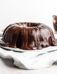 A chocolate frosting covered Chocolate Buttermilk Bundt Cake on a white plate against a white background.