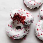 White chocolate topped red velvet donuts with valentines day sprinkles overtop.