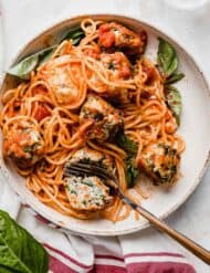 Marinara coated spaghetti noodles on a white plate topped with turkey spinach meatballs.