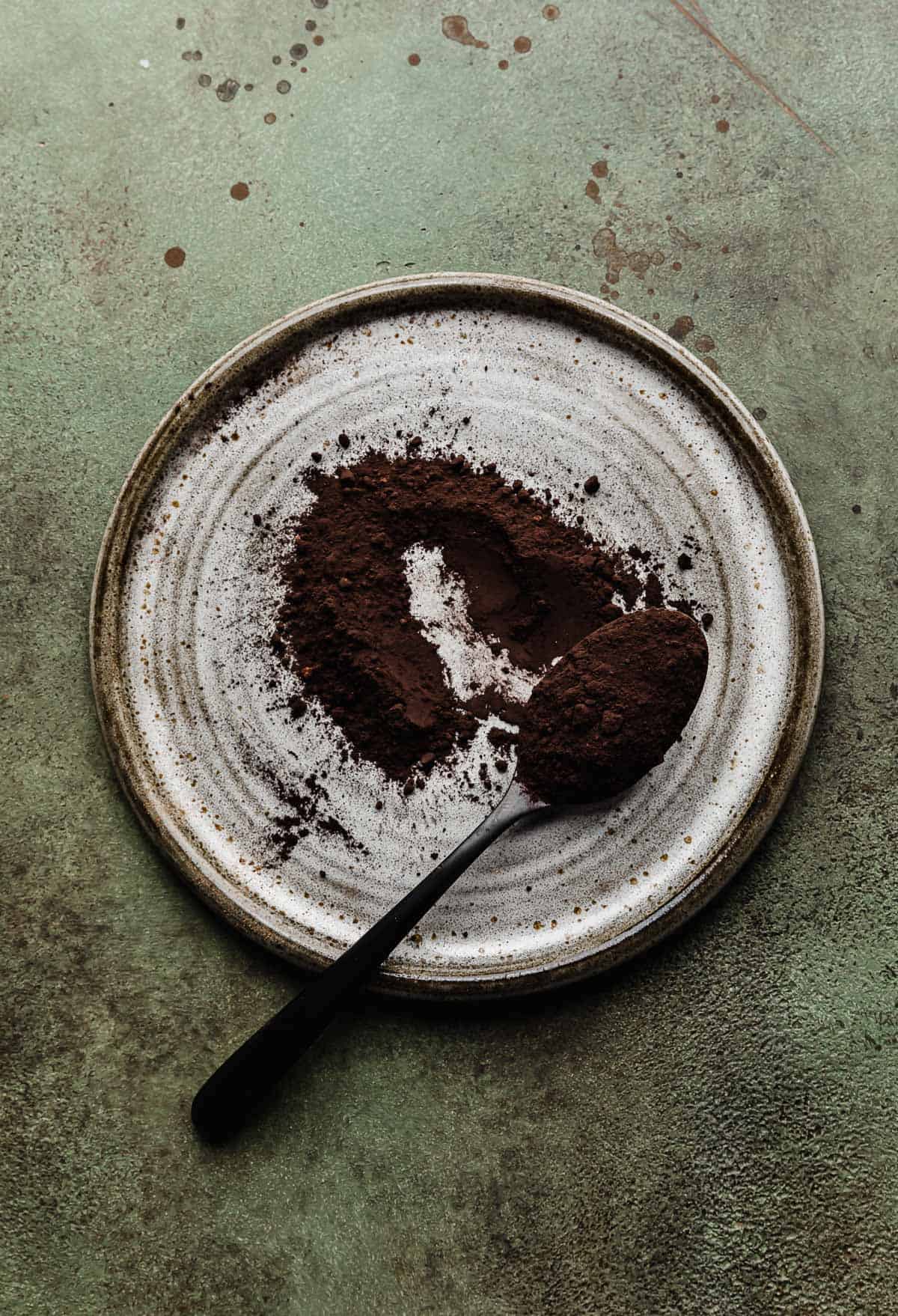 A gray plate with a scoop of black cocoa powder on it.