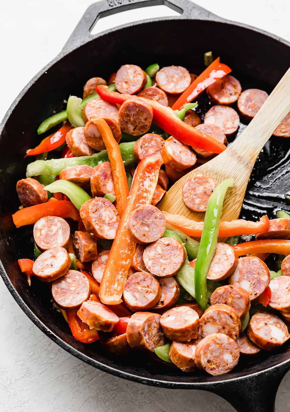 A black skillet with red and green sliced peppers and sliced sausages in it.