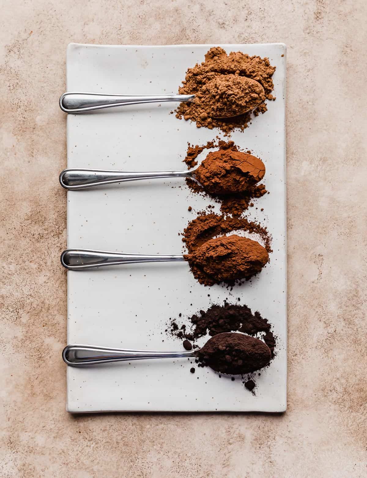 Four cocoa powders on separate spoons on a rectangular white plate.