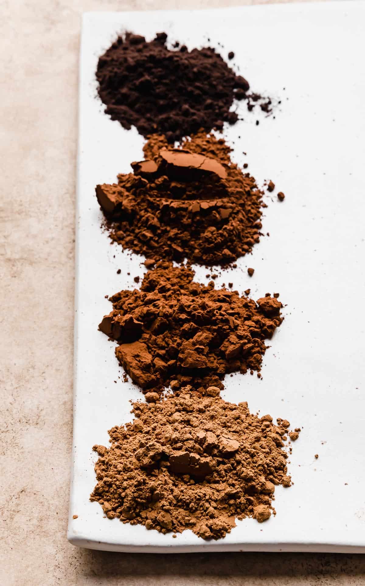 Small piles of different cocoa powders on a white plate.