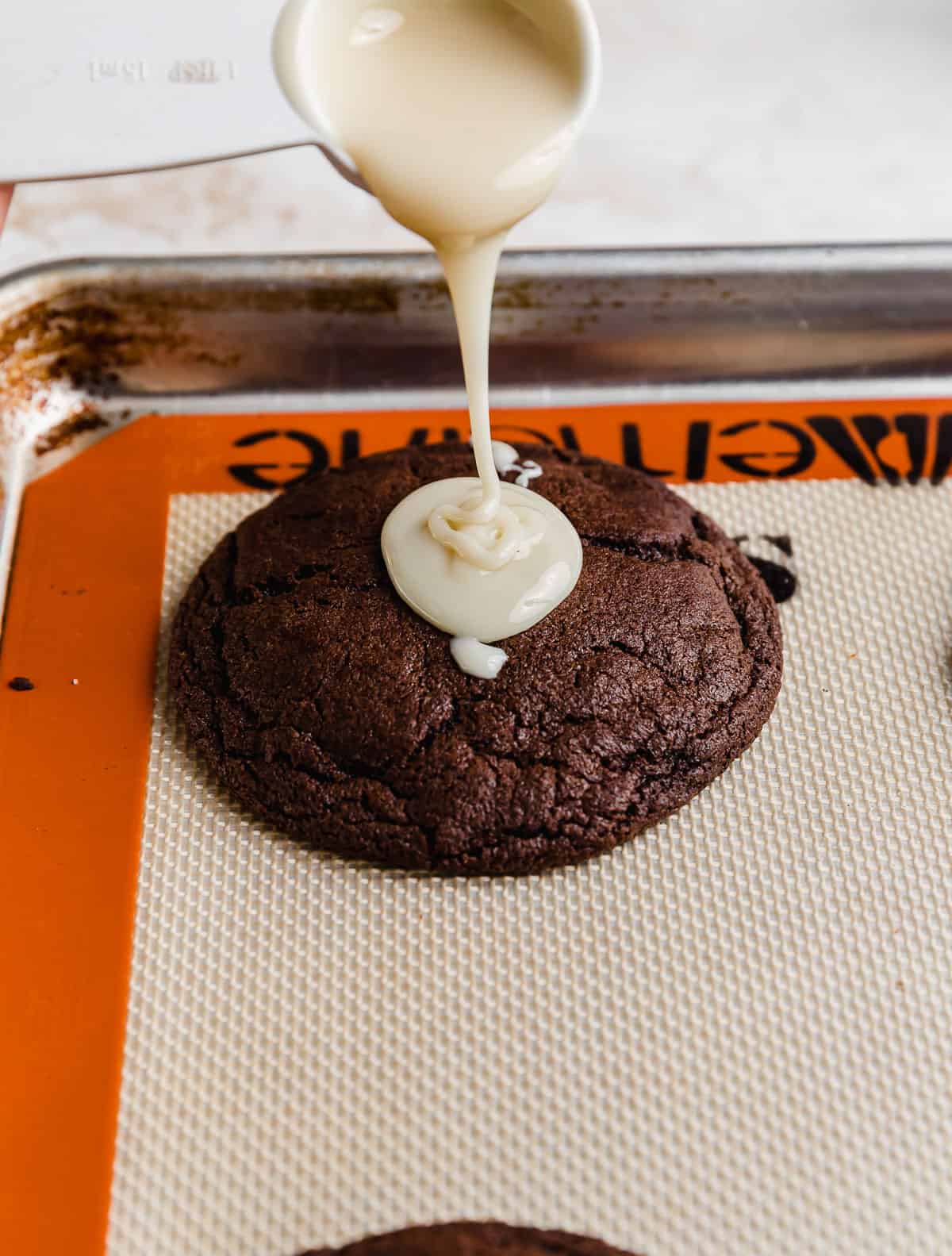 Sweetened condensed milk being poured overtop a chocolate cookie.
