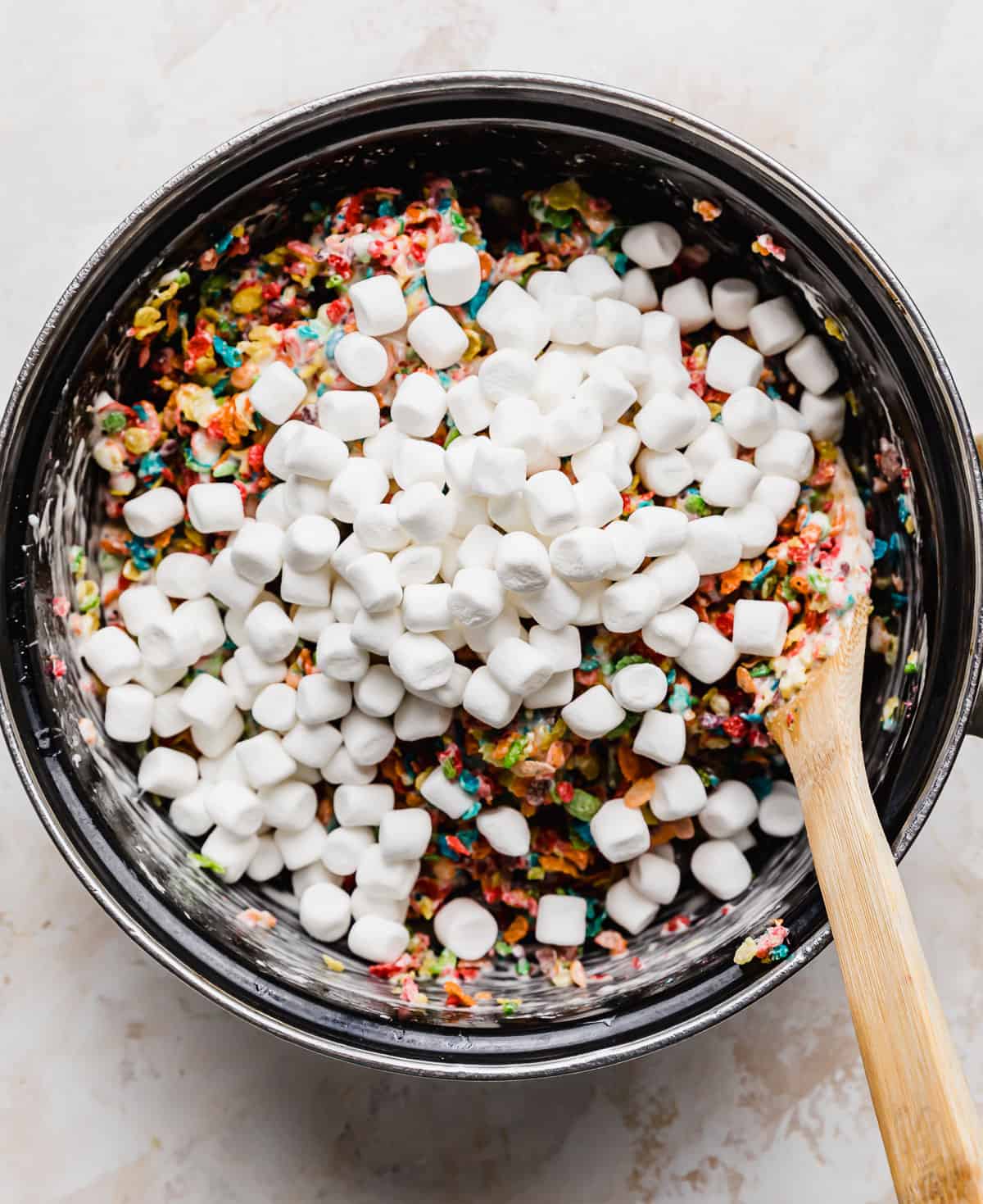 Mini marshmallows overtop Fruity Pebble Rice Krispie Treat mixture in a pot.