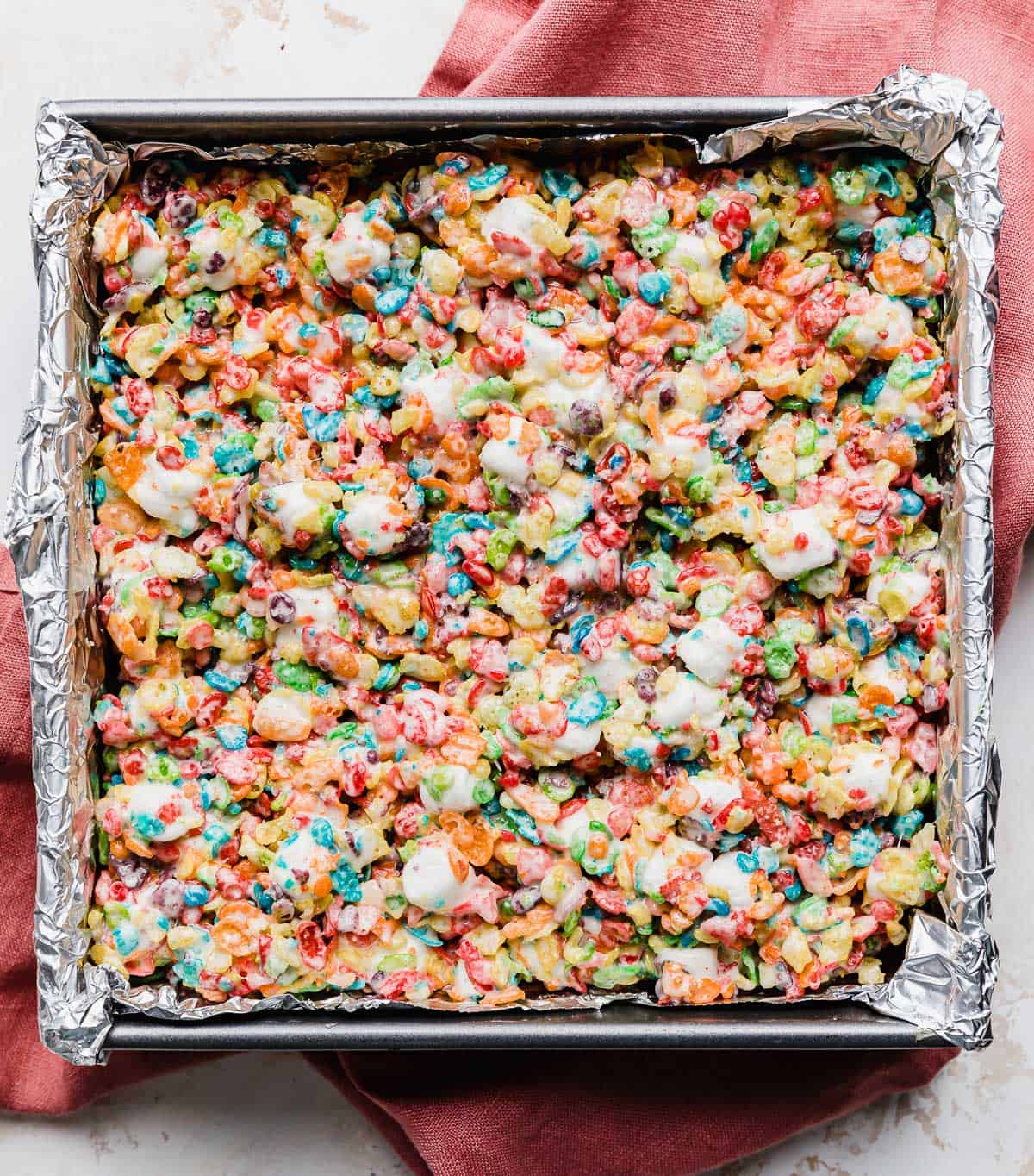 A square pan lined with foil and filled with Fruity Pebble Rice Krispie Treats.