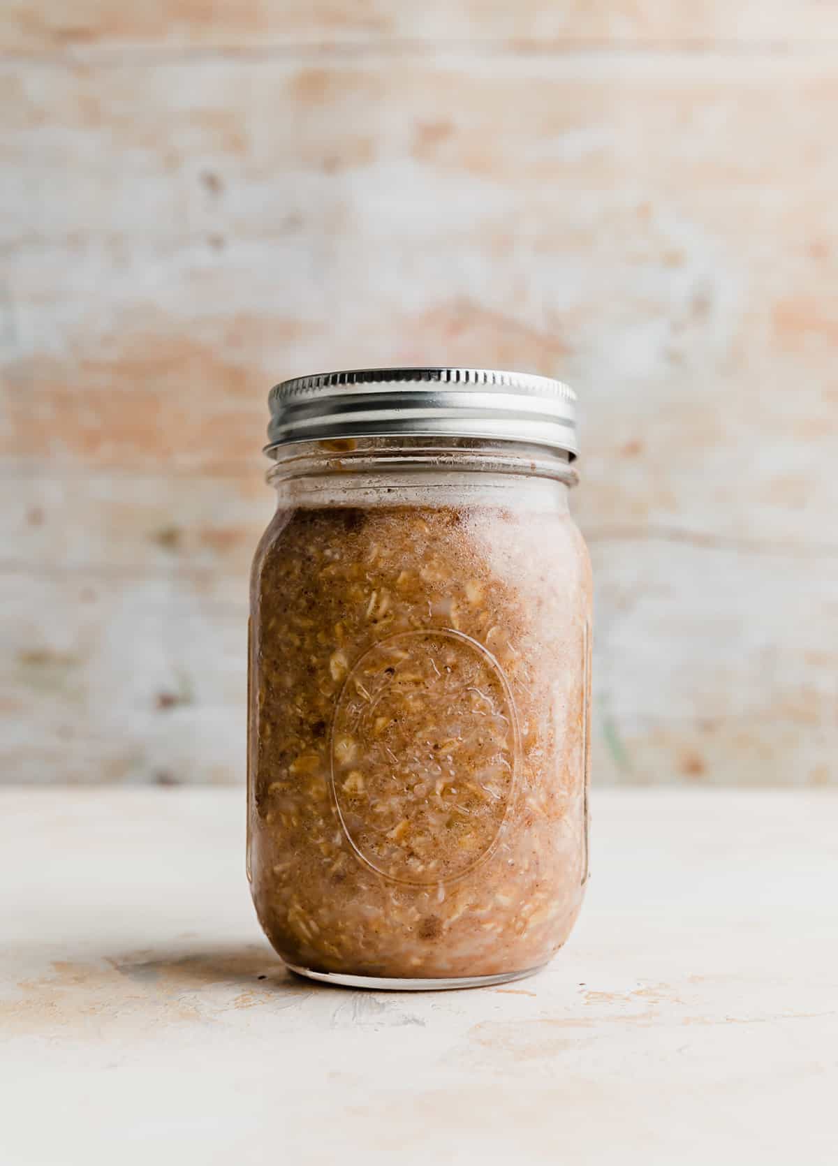 A glass jar full of light brown High Protein Overnight Oats with a metal lid on top.