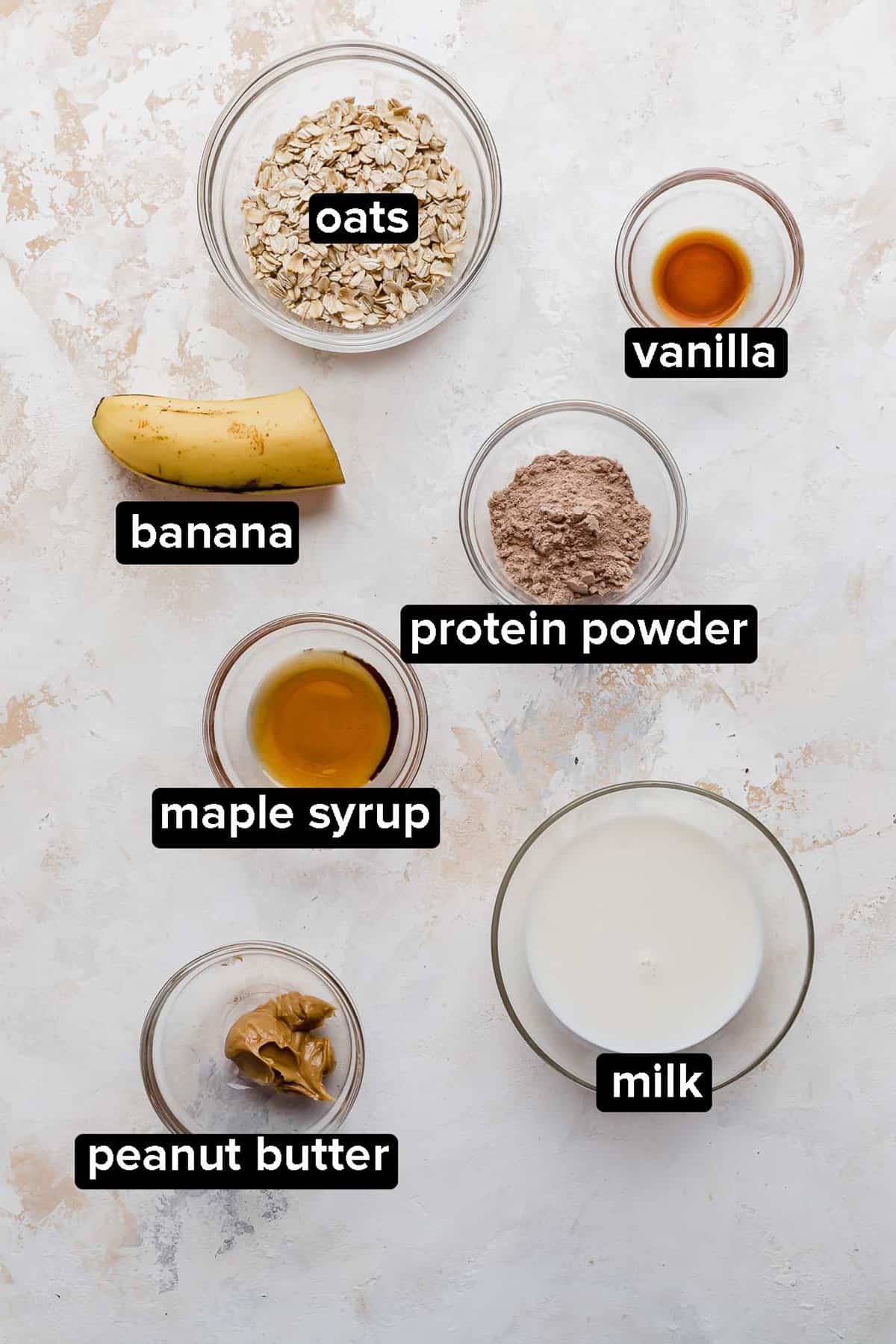 High Protein Overnight Oats ingredients in a glass bowl on a textured white and cream background.