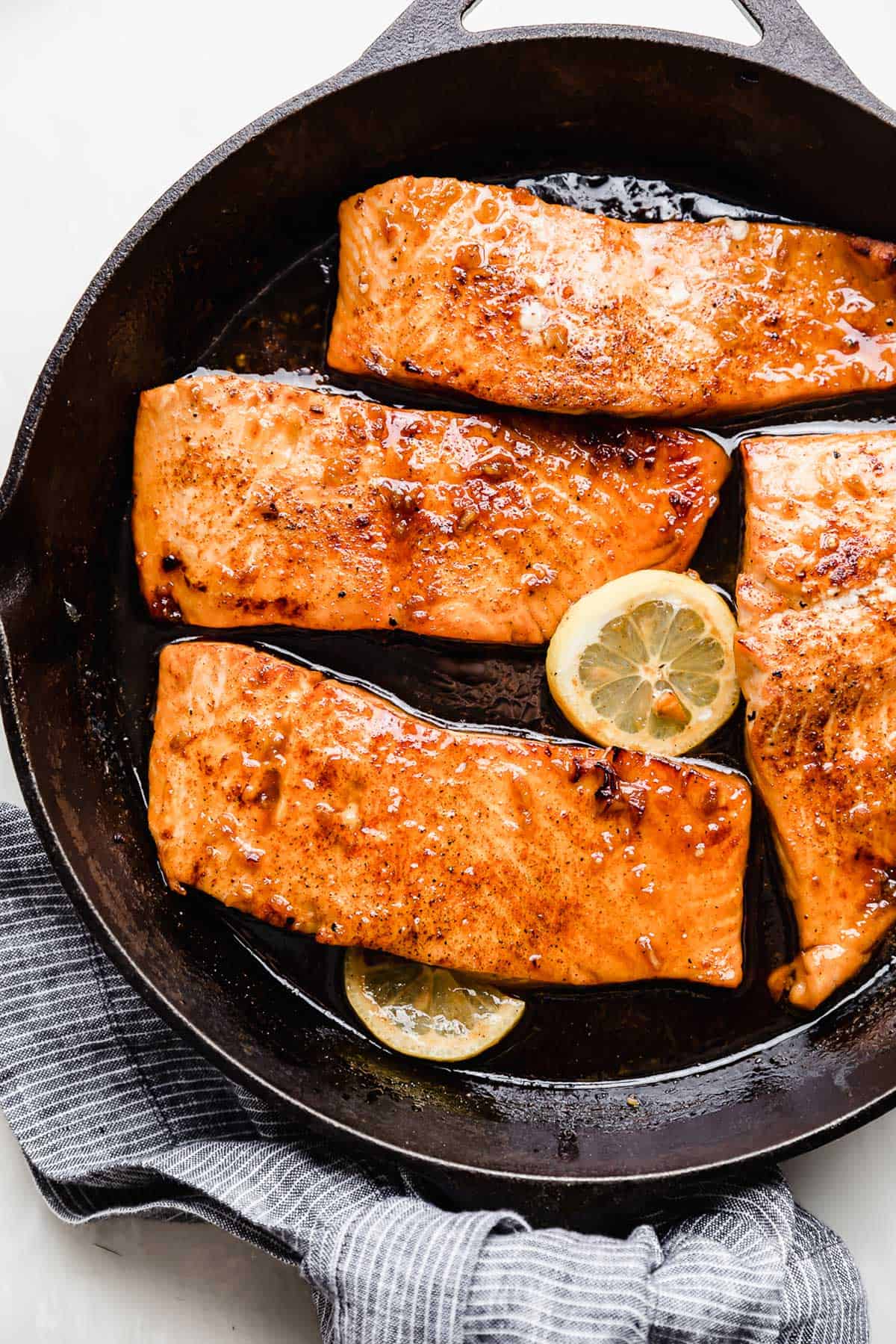 Honey Garlic Salmon filets in a cast iron skillet with slices of lemon surrounding each filet.
