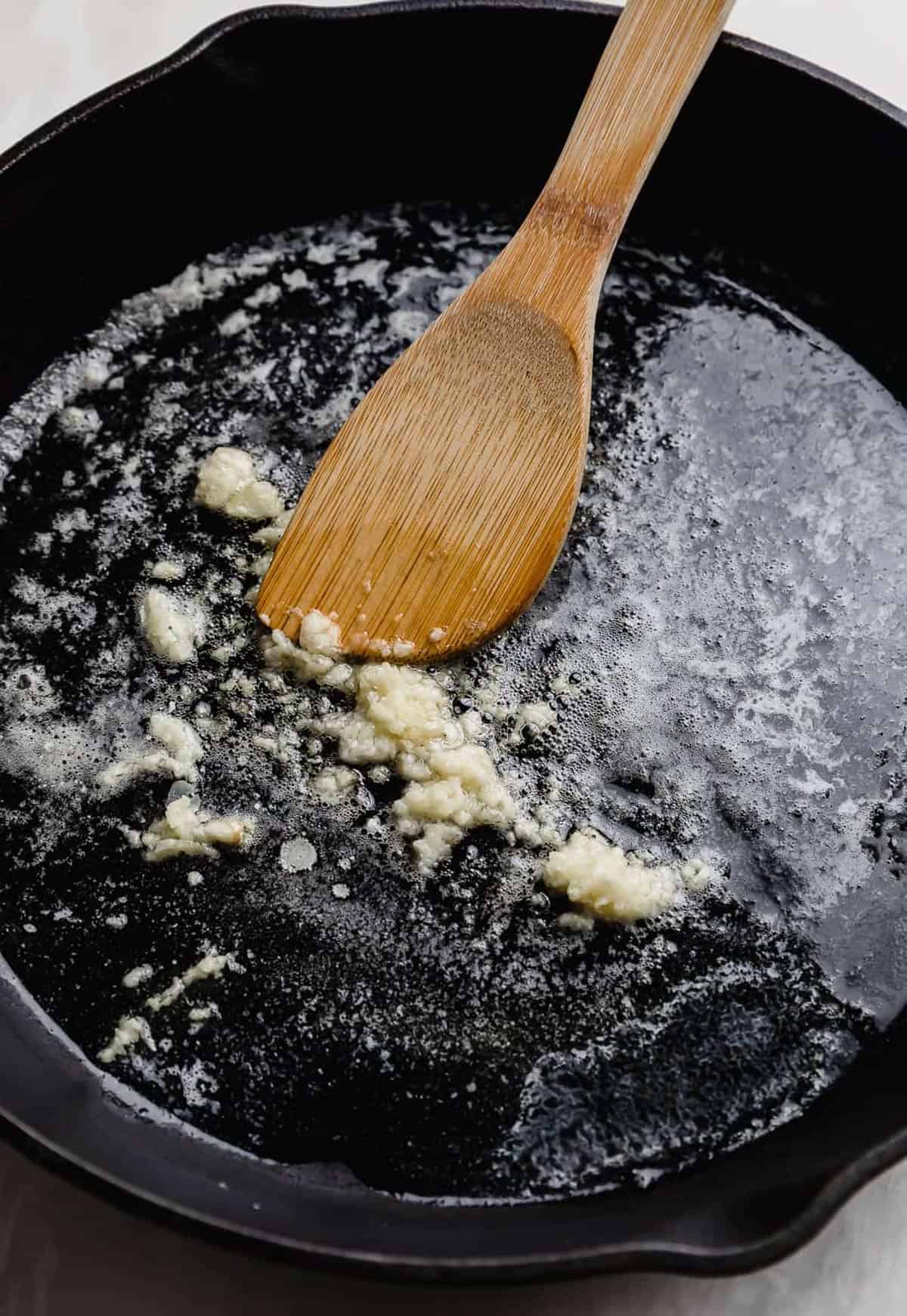 A wooden spoon stirring minced garlic in a cast iron skillet.