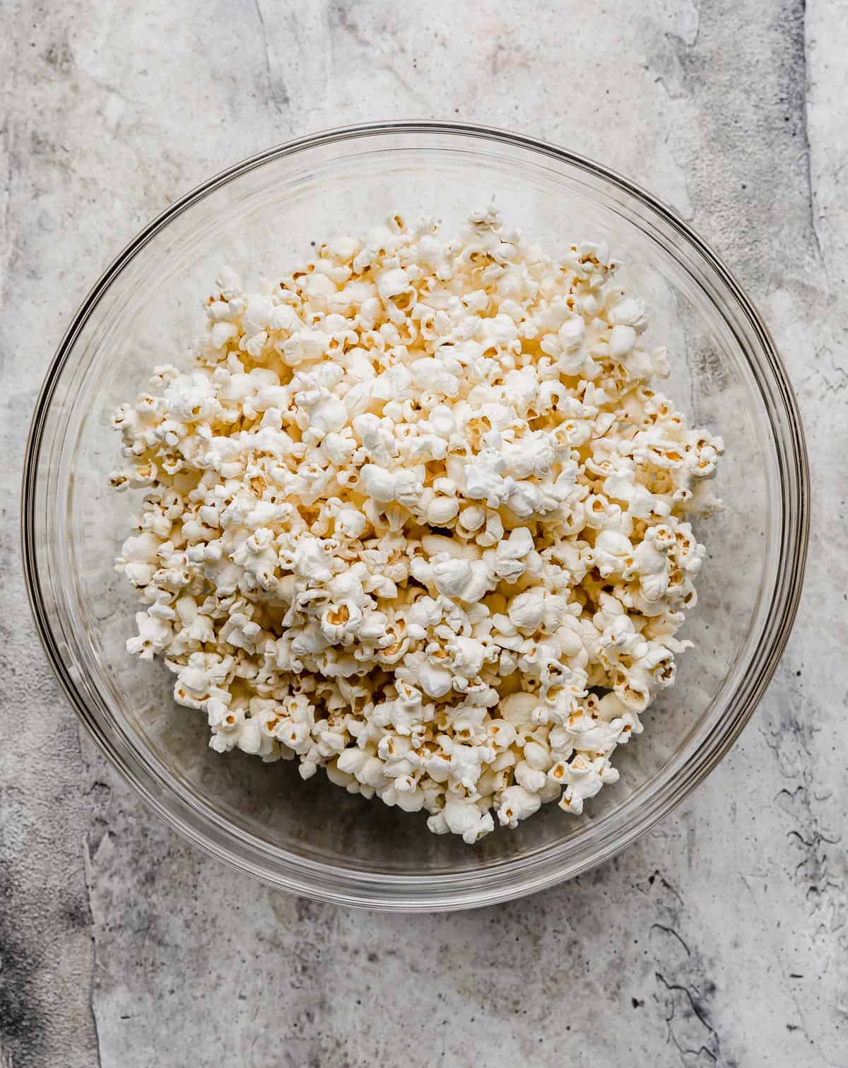 Popped popcorn in a glass bowl on a gray background.