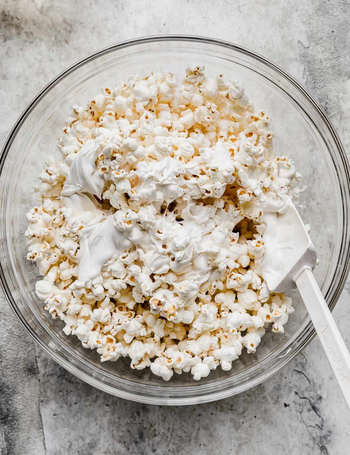 White chocolate covered popcorn (making Oreo Popcorn) in a glass bowl.