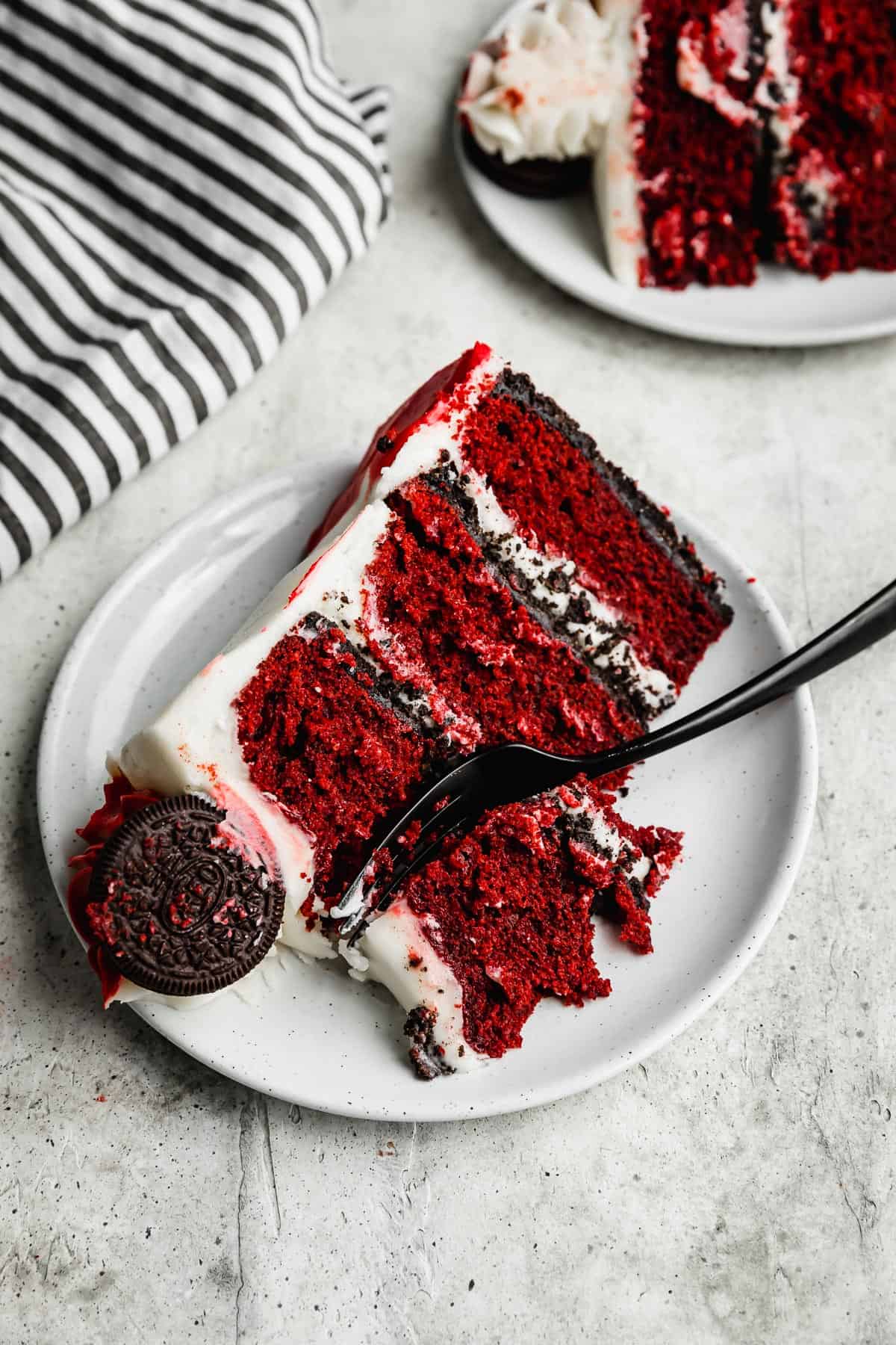 A slice of Oreo Red Velvet Cake on a white plate with a black fork cutting into it.