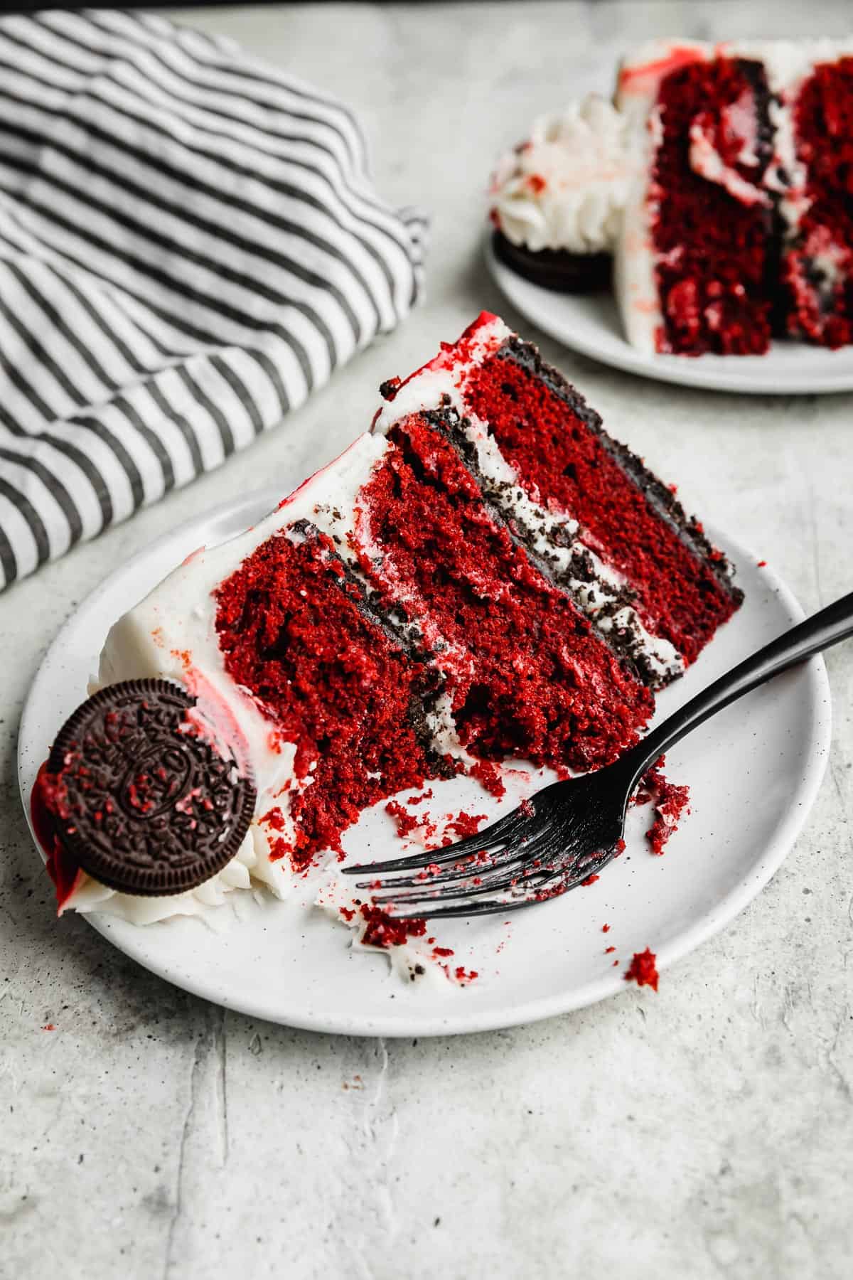 A slice of Oreo Red Velvet Cake on a white plate with a black fork next to it.