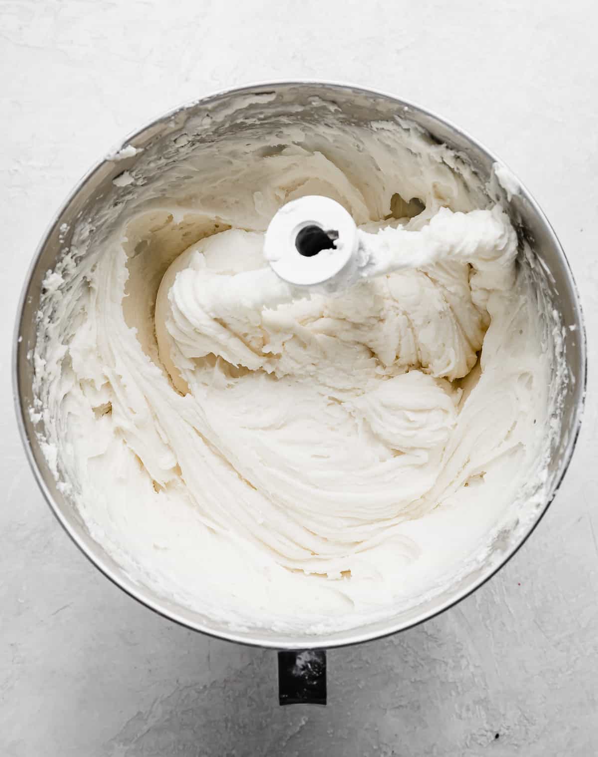 A metal mixing bowl with white cream cheese frosting in it.