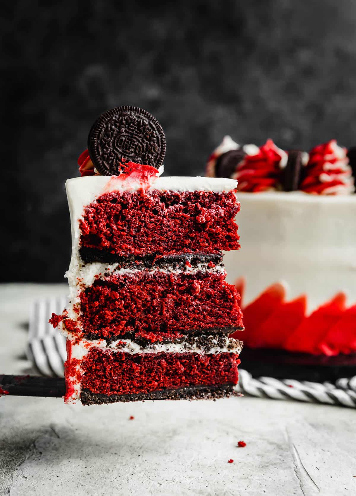 A slice of Oreo Red Velvet Cake baked on an oreo crust topped with cream cheese frosting.