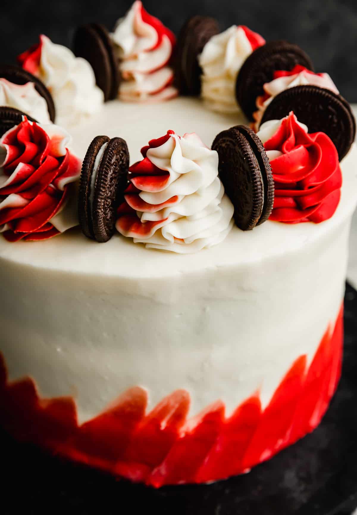 A red and white frosted Oreo Red Velvet Cake with red and white frosting swirls on the top and Oreo cookies between each swirl.