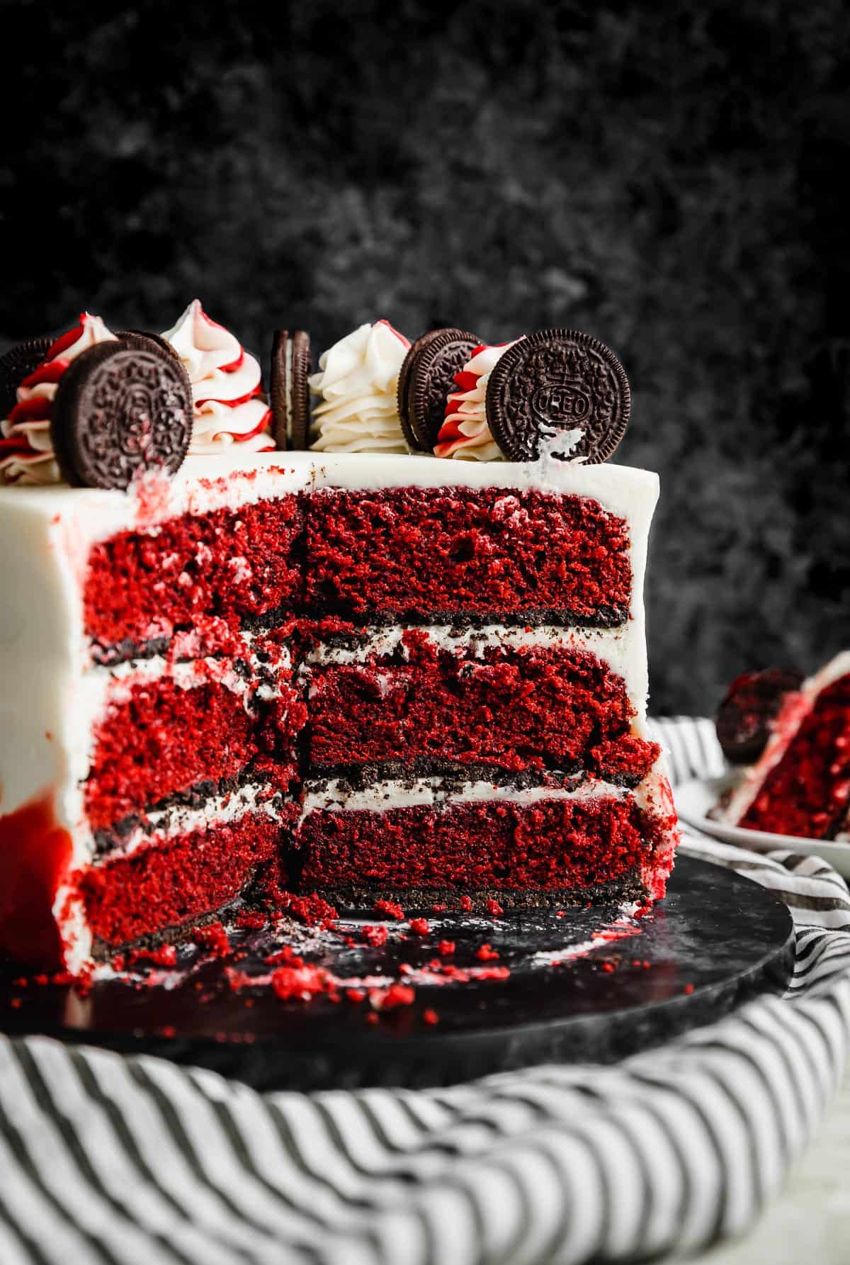 Three tiered Oreo Red Velvet Cake baked on an oreo crust with white cream cheese frosting.