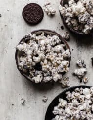Oreo crumbs and white chocolate covered popcorn in a black bowl on a gray textured background.