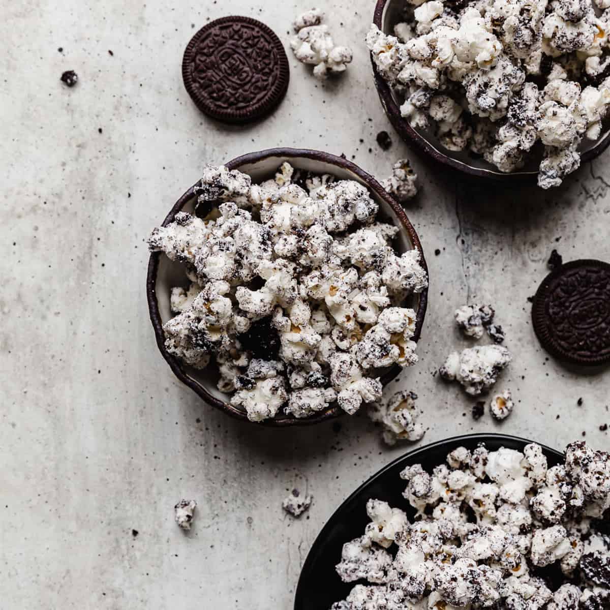 Oreo crumbs and white chocolate covered popcorn in a black bowl on a gray textured background.
