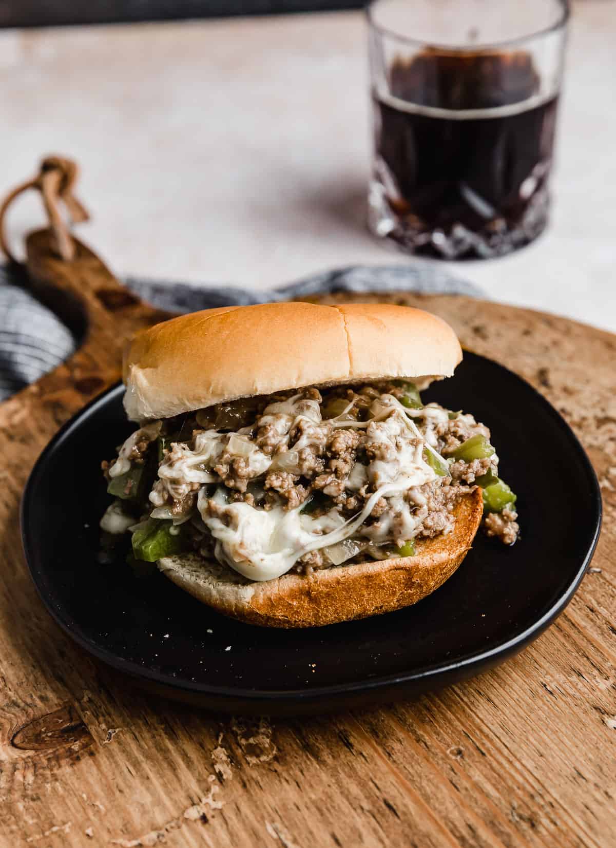 A Philly Cheesesteak Sloppy Joe on a black plate on a wooden round cutting board.