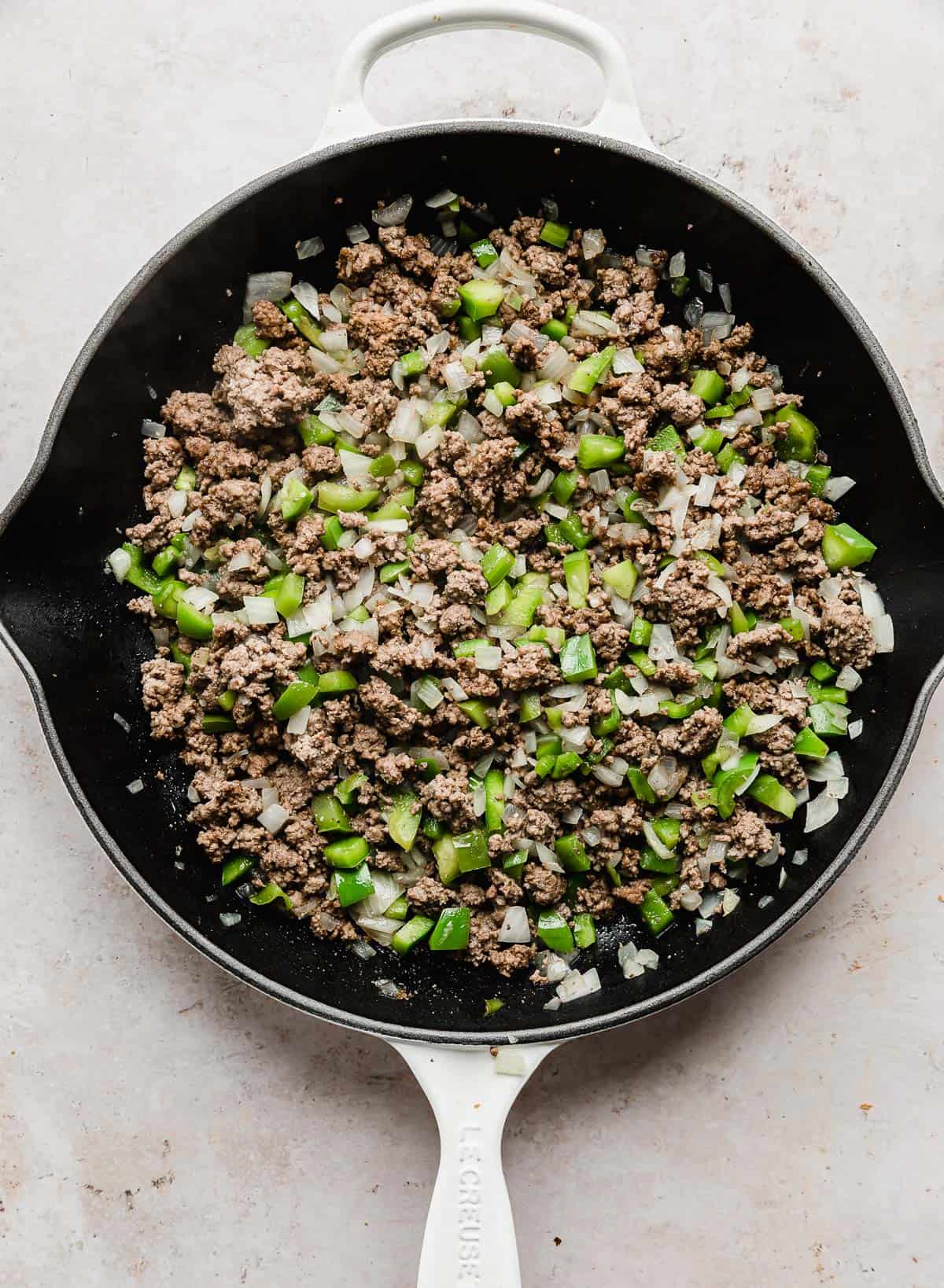Ground beef mixed with chopped onion and green peppers in a skillet.