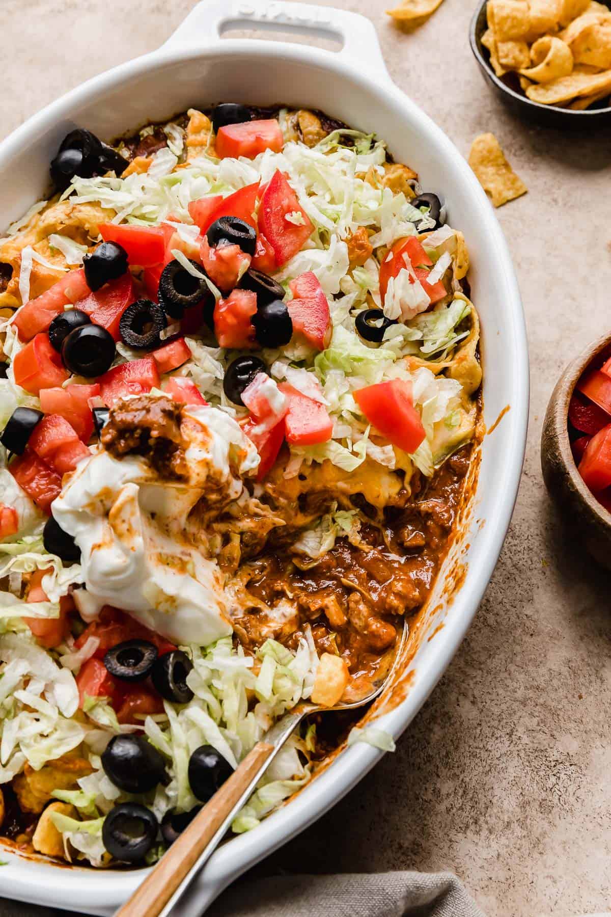 A close up photo of a spoon scooping out some Walking Taco Casserole from a white round baking dish.