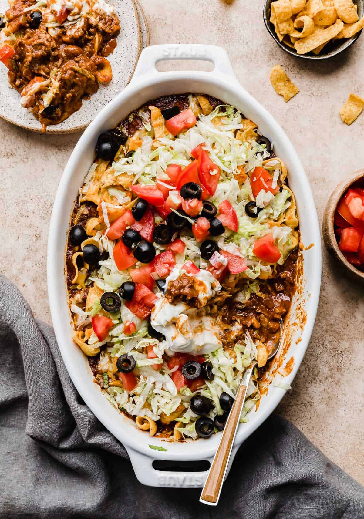 An overhead photo of a Walking Taco Casserole Recipe baked in an oval white dish, that's on a beige textured background.