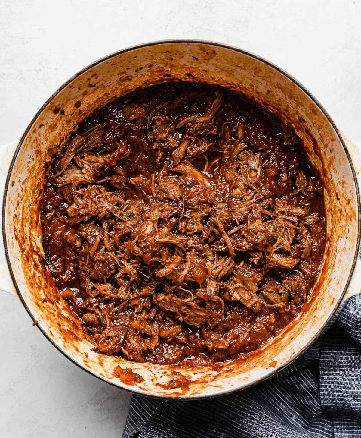 A shredded beef Ragu sauce in a white pot on a white background.