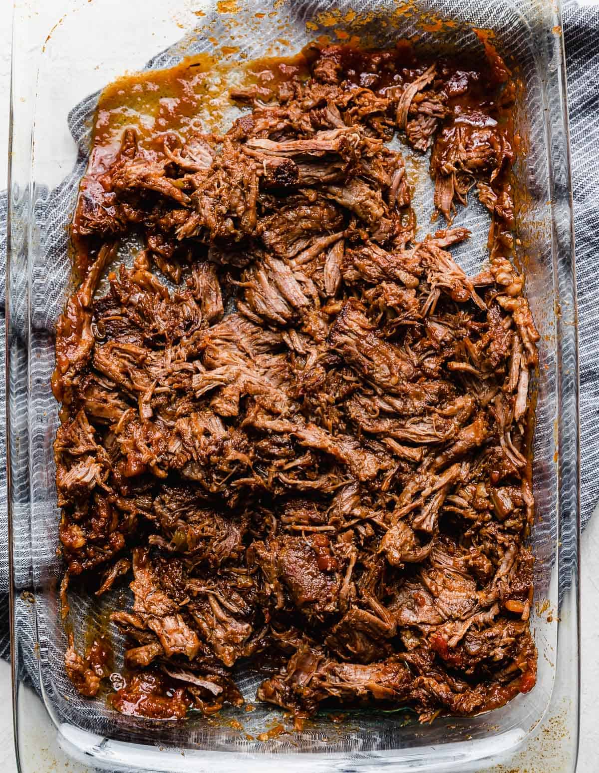 Shredded beef in a glass baking dish for making the best beef Ragu recipe.