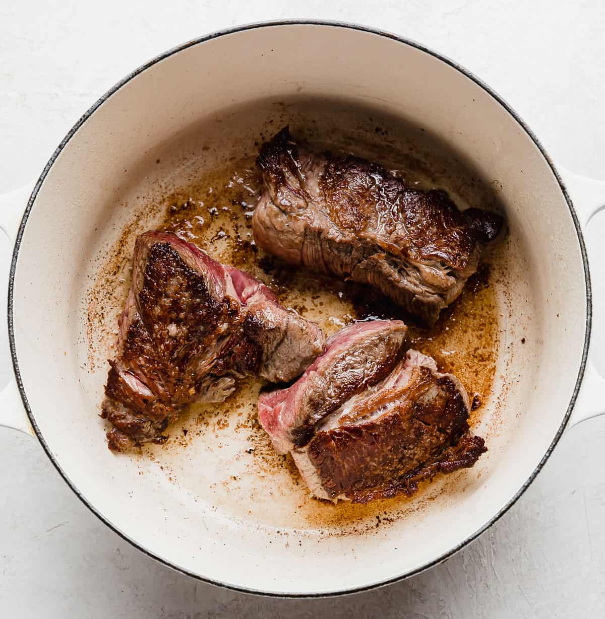 Three seared beef chuck roasts in a white pot.