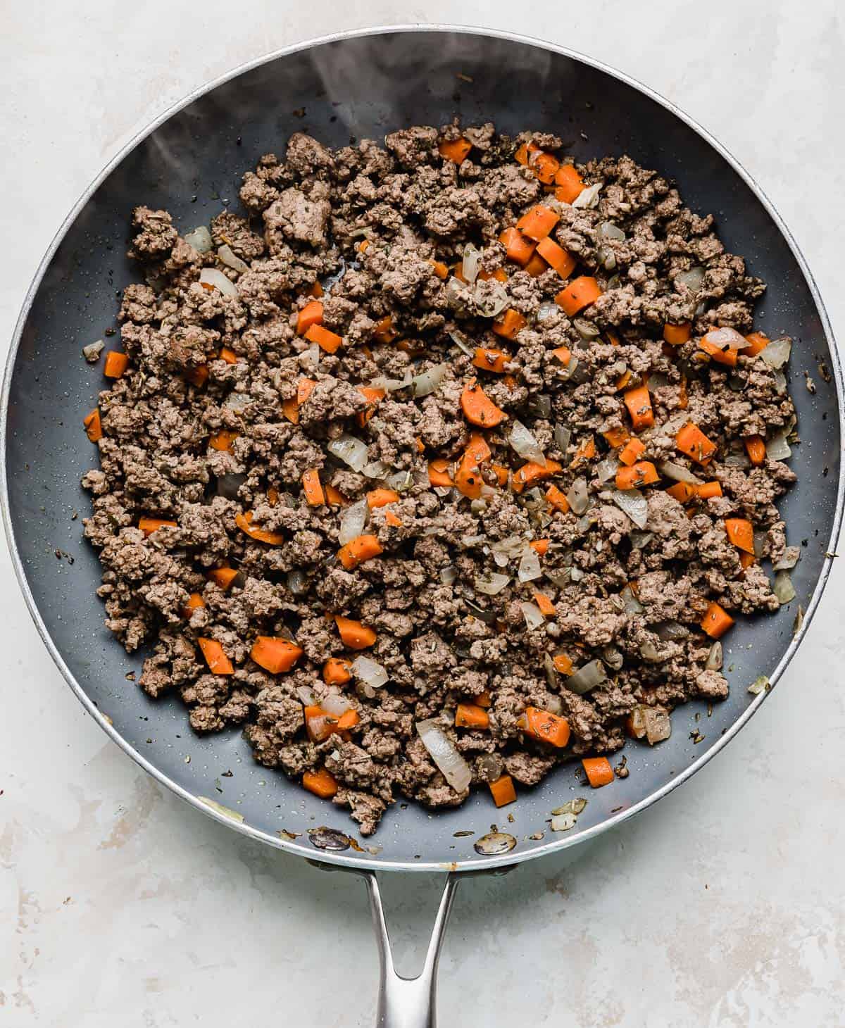 Shepard's pie ground beef mixture with carrots and onion in a skillet.