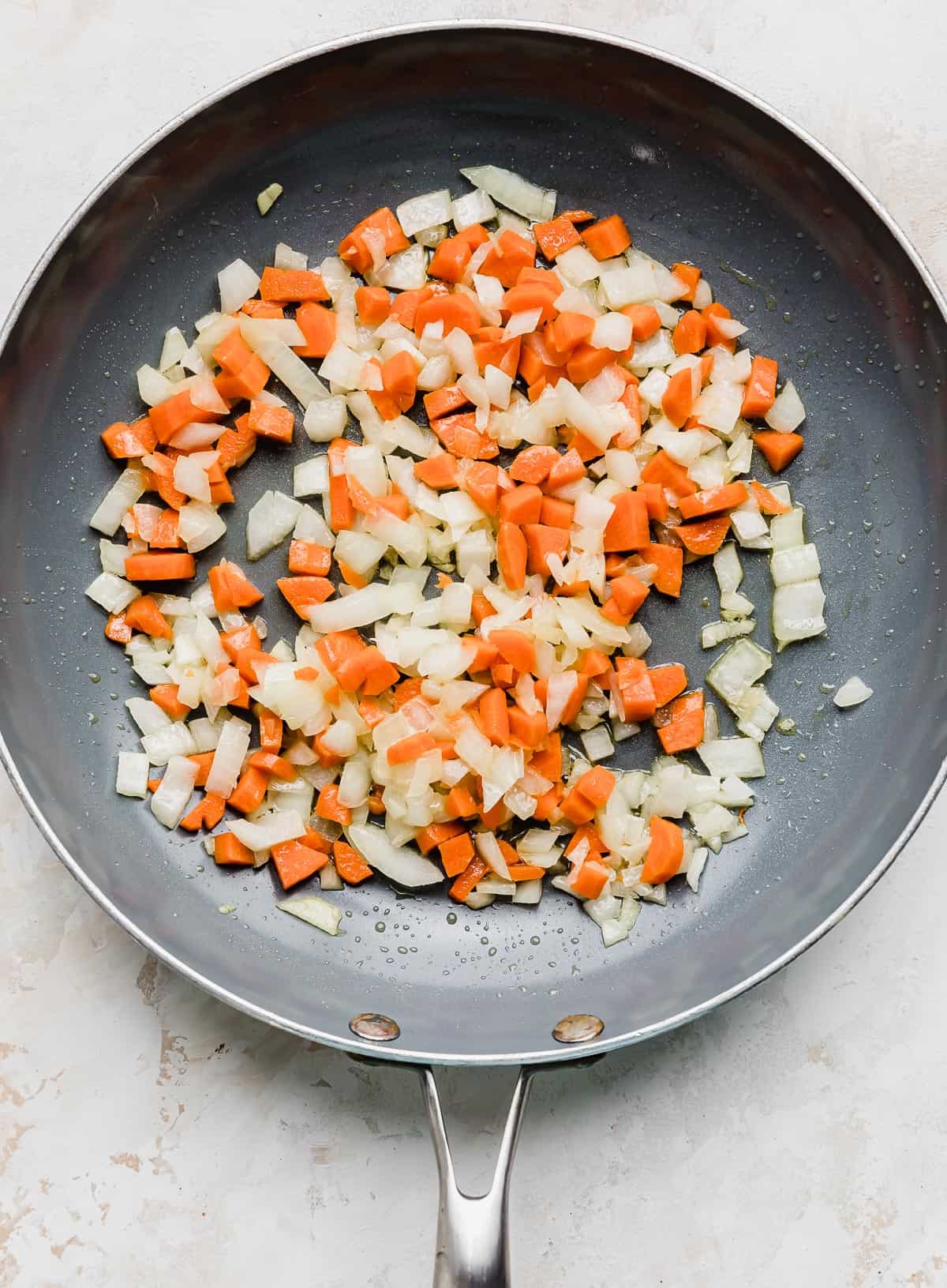 A gray skillet with cooked diced carrots and onion in it.