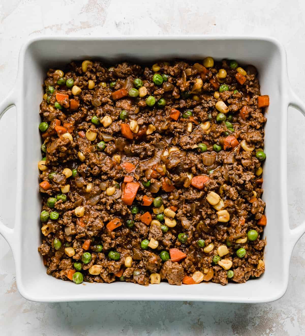 A white square baking dish filled with ground beef Easy Shepherd's Pie mixture.