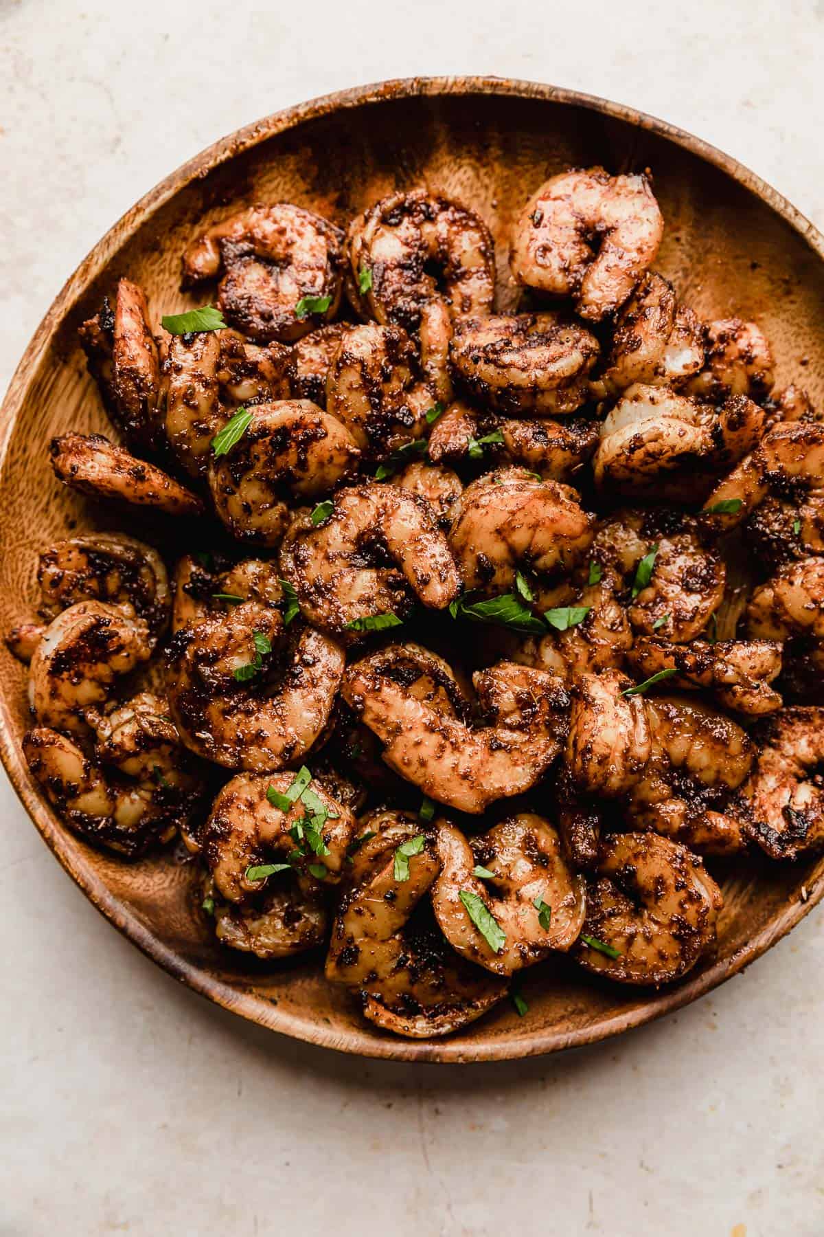 A wood plate on a white background, with cooked Blackened Shrimp on the plate and chopped parsley for garnish.