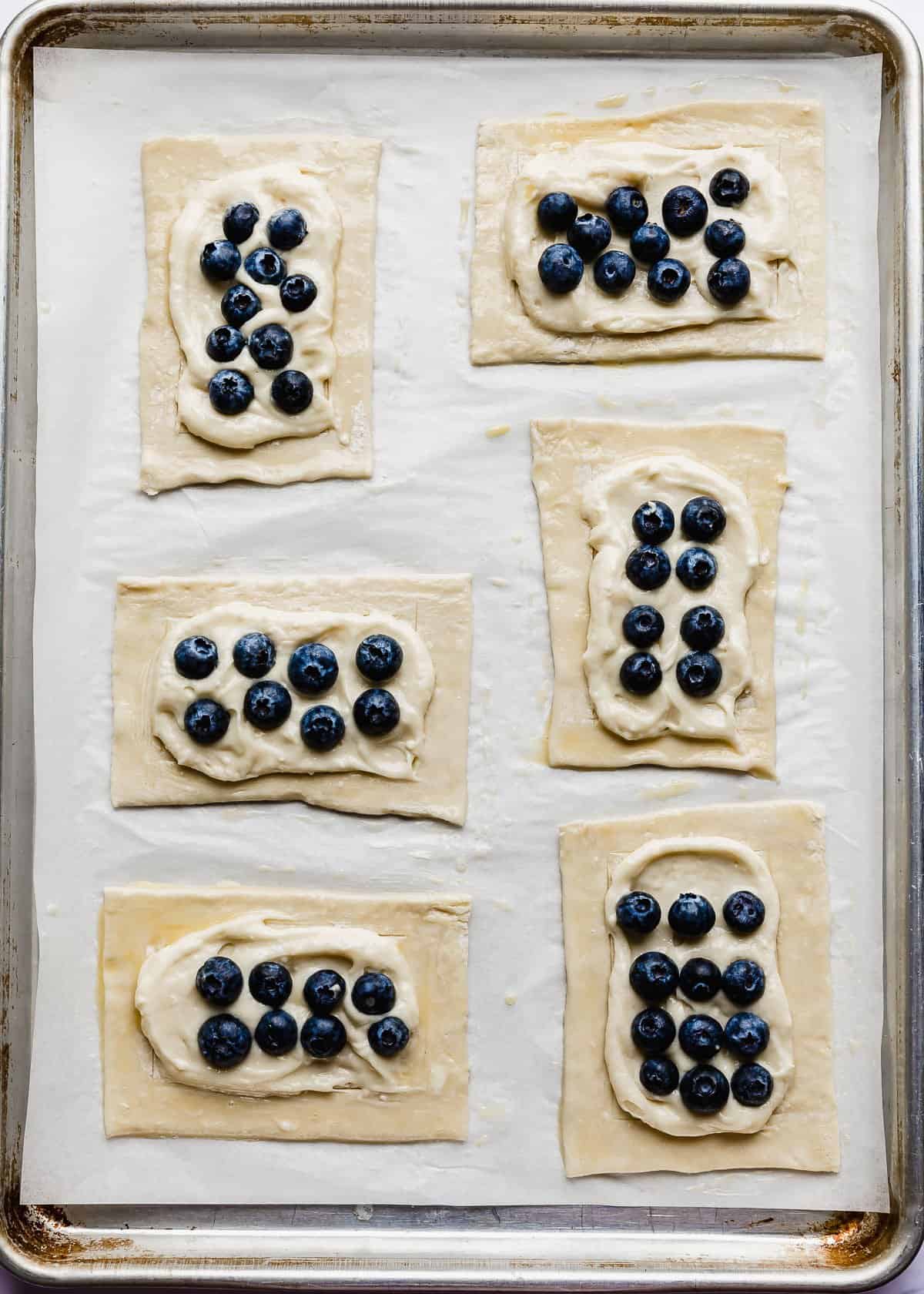 Fresh blueberries on top of a cream cheese mixture on raw puff pastry squares.