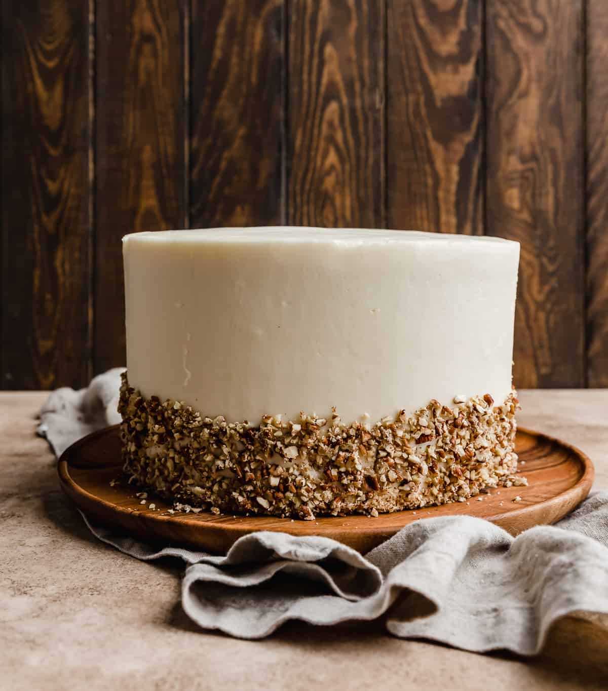 A layered carrot cake with cream cheese frosting and chopped pecans along the bottom third of the cake. 