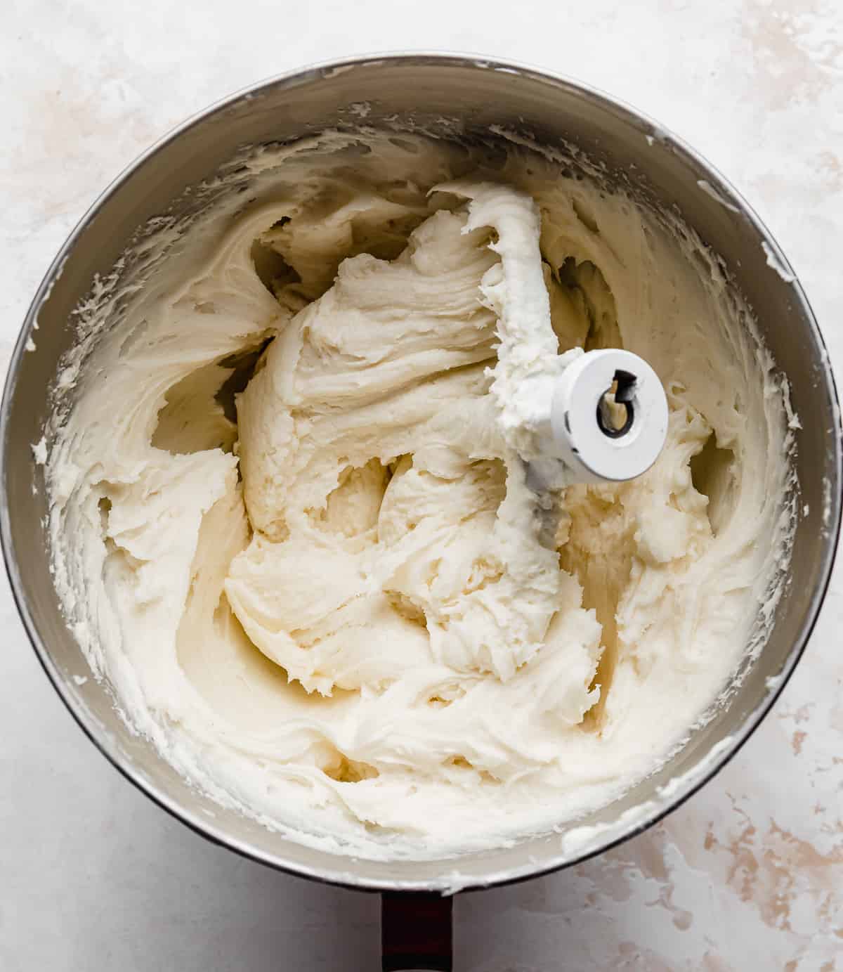 A metal bowl filled with white cream cheese frosting against a white background.