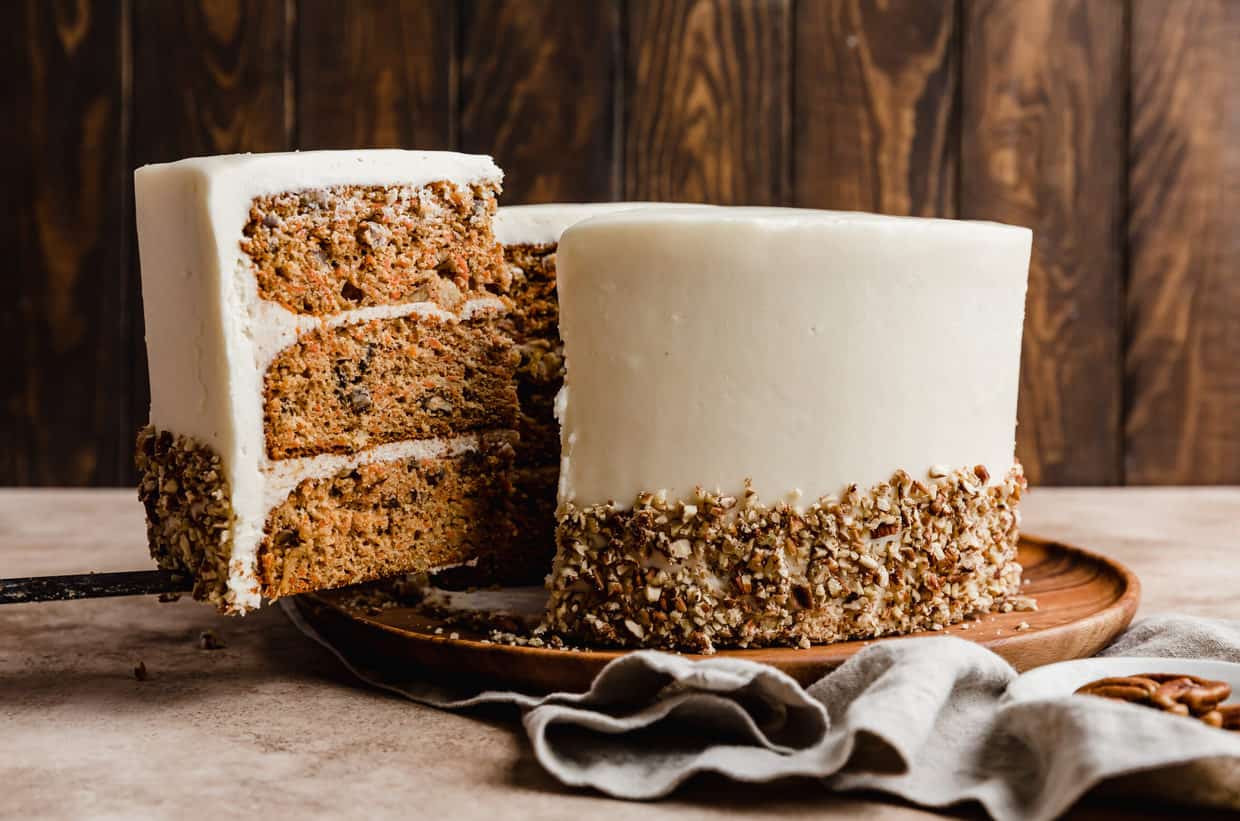 A slice of moist carrot cake topped with cream cheese frosting being lifted from the main Carrot Cake recipe.