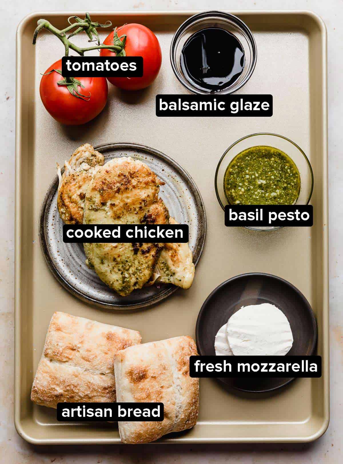 Ingredients used to make a Chicken Caprese Sandwich spread on a bronze baking sheet. 