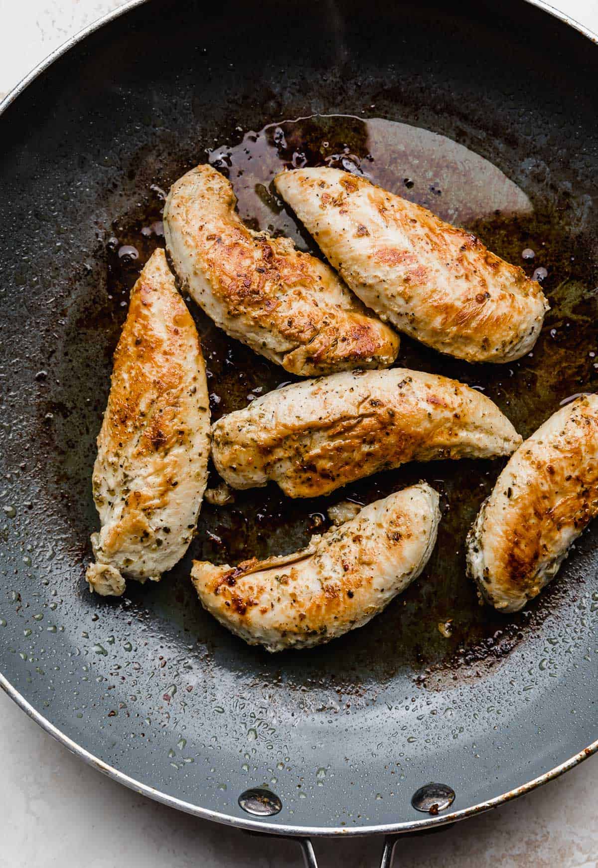 A skillet with seasoned greek chicken tenders for making easy chicken gyros.