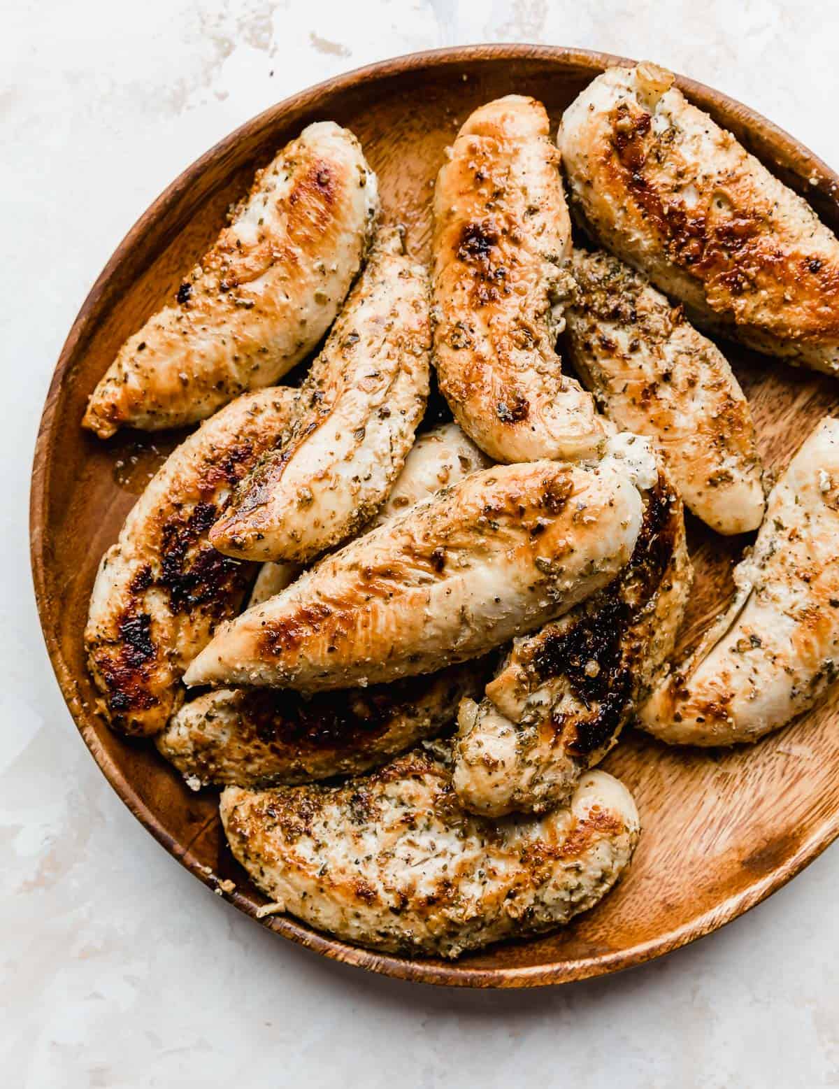 A brown plate with golden brown cooked chicken tenders on it, on a white background.