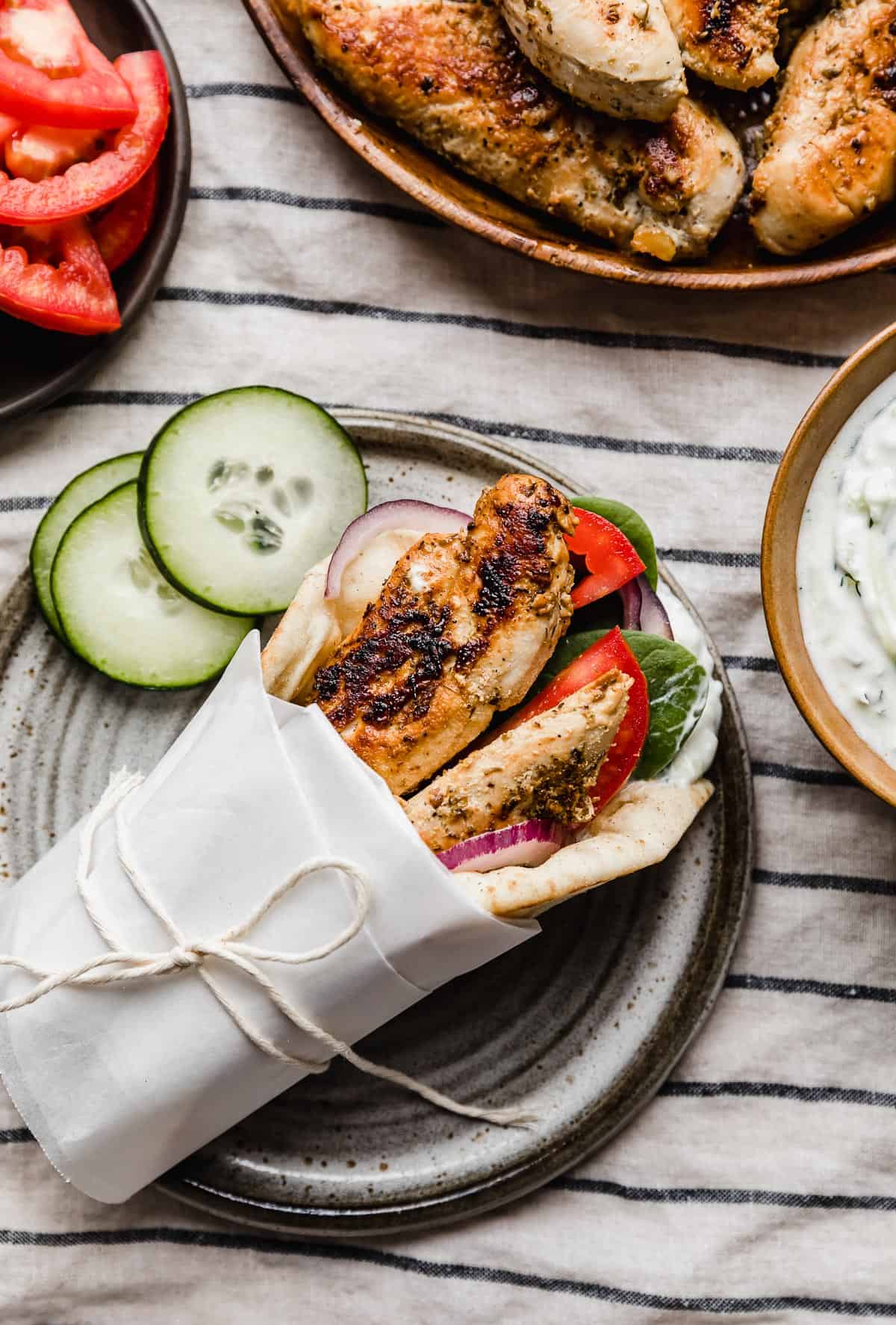 White parchment and kitchen twine wrapped around chicken tender Greek gyro on a gray plate against a white and blue striped napkin.
