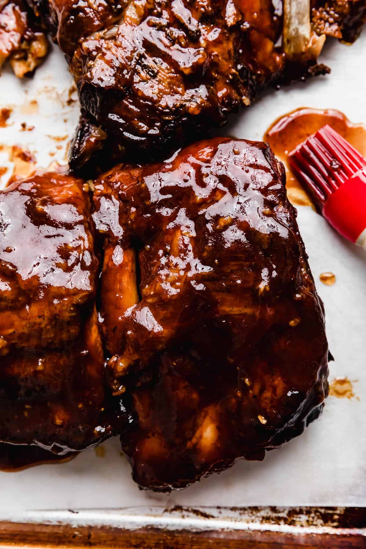 Coca Cola Ribs covered in a dark brown and red colored sauce on a white background.