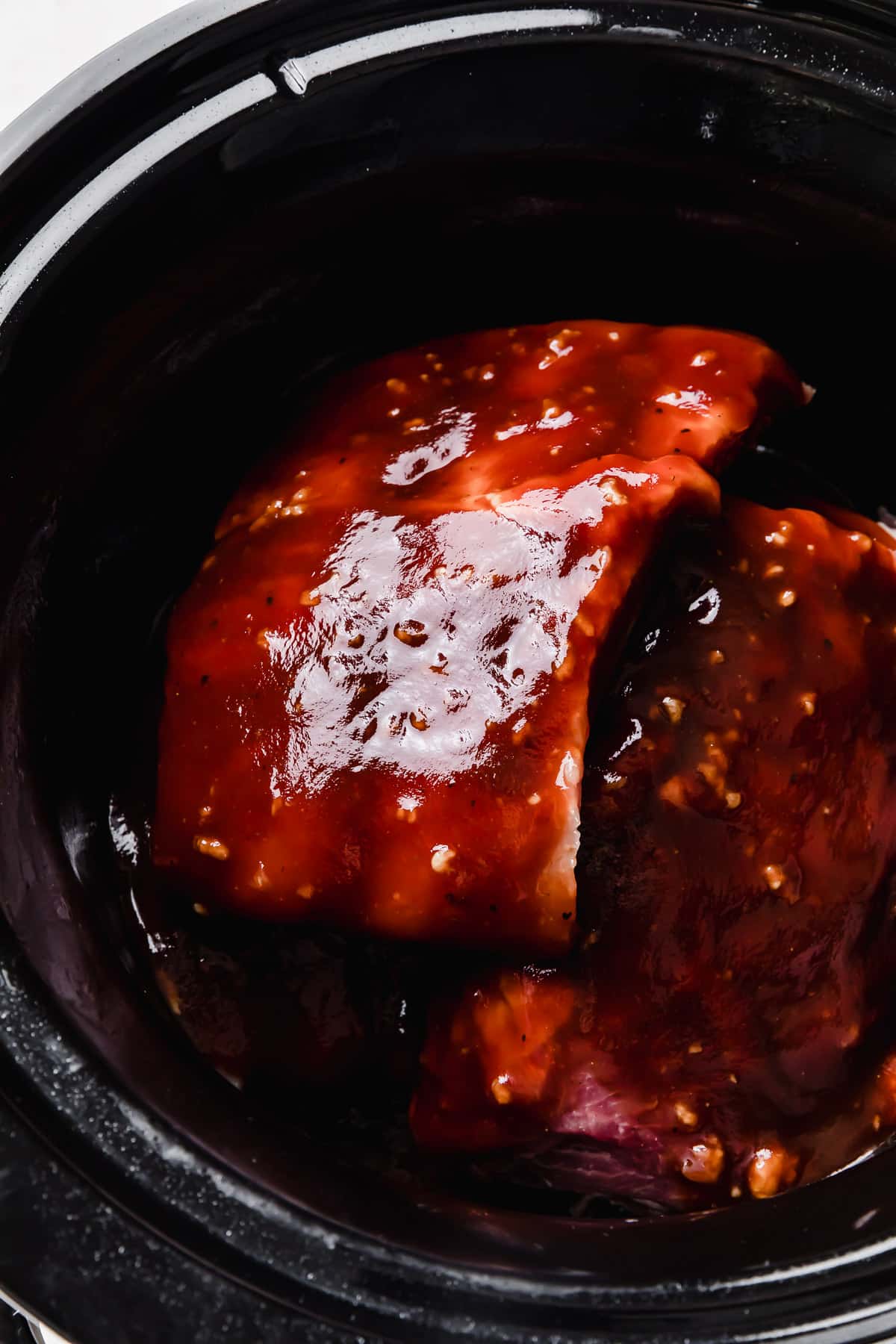 A dark brown and red colored sauce made with barbecue sauce and Coca Cola overtop ribs.