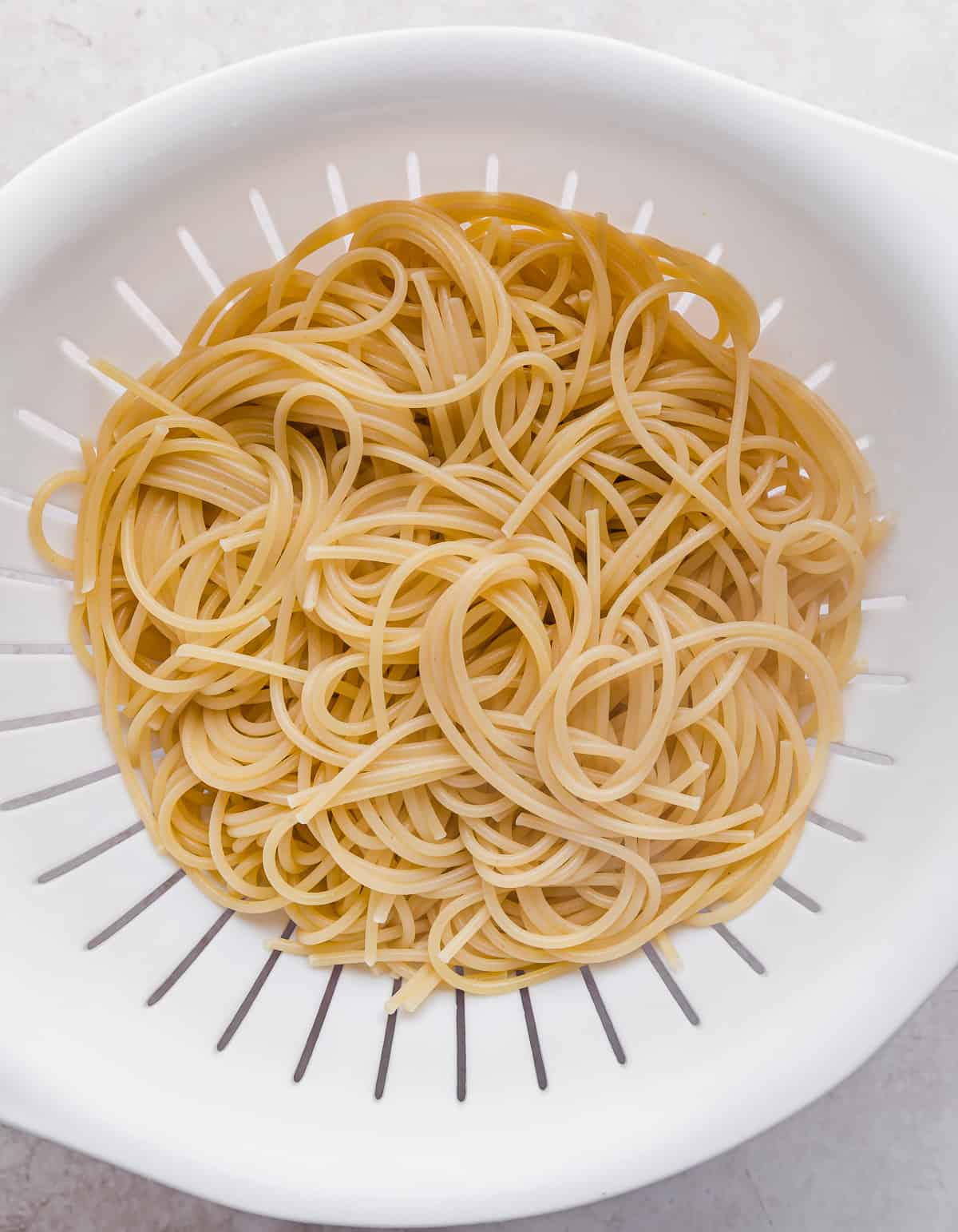 A white colander with cooked and drained spaghetti noodles in it.