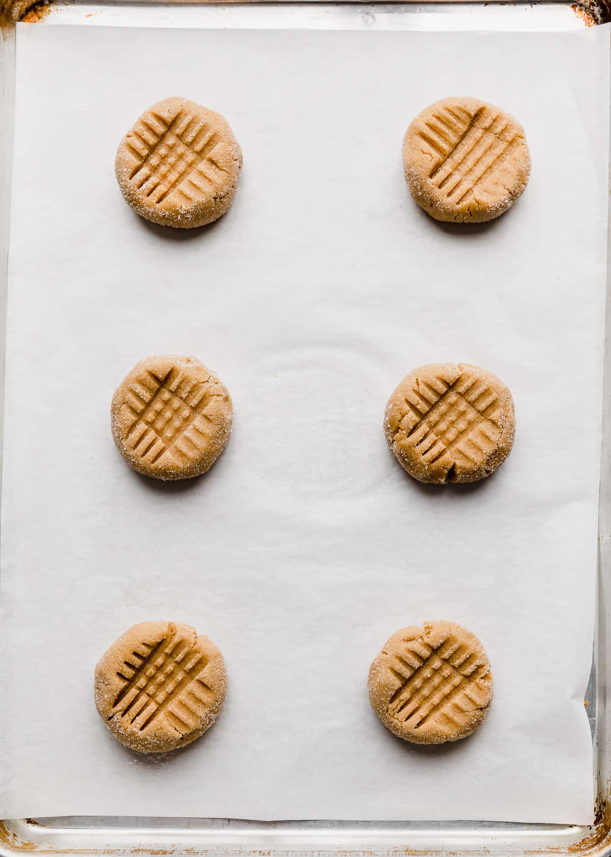 Six copycat Crumbl Classic Peanut Butter Cookies on a white parchment lined baking sheet.