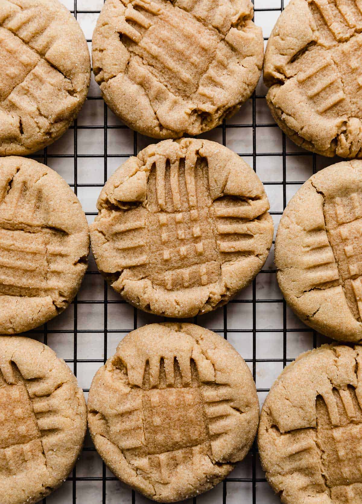 Criss cross imprinted Classic peanut butter cookies lined up on a black wire cooling rack.