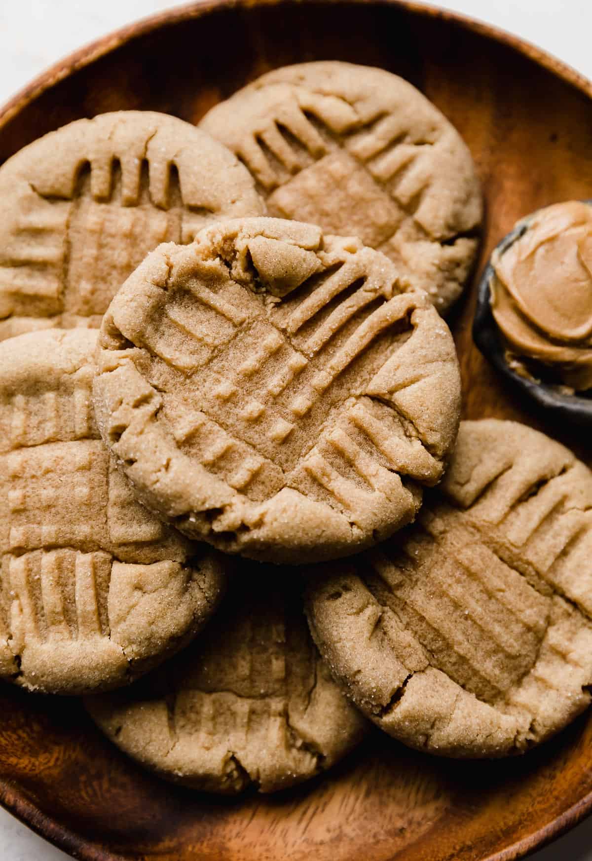 A brown plate with copycat Crumbl Classic Peanut Butter Cookies on it with a criss cross fork imprint in each cookie.